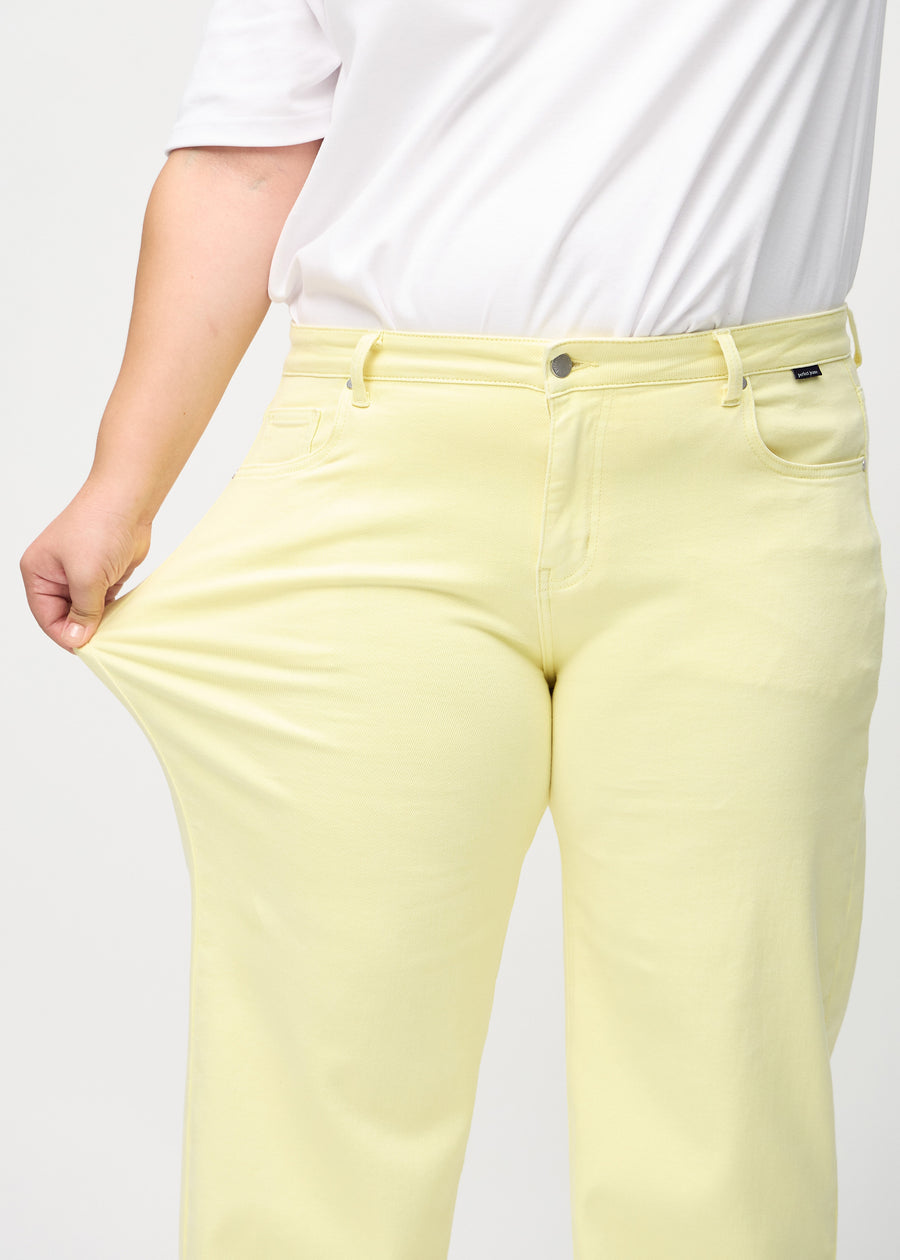 Plus-size model strækker jeansene ved låret for at vise stretch.
