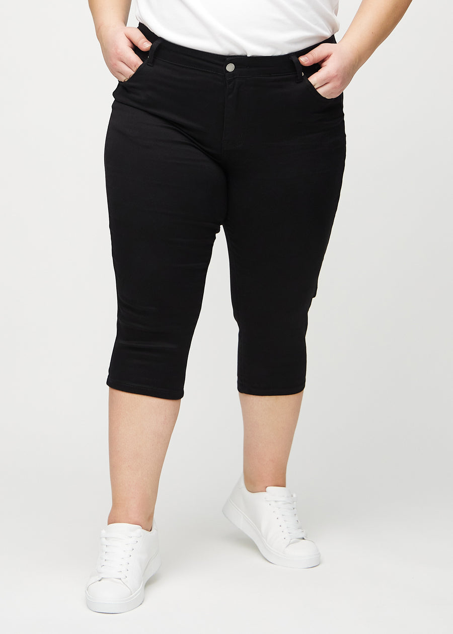 Sorte skinny capris, modelnavn Ravens, som sidder tæt til benet og slutter lige under knæet på en plus-size model, set forfra.
