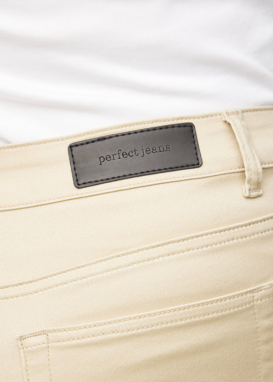 Close-up of beige jeans material with the Perfect Jeans leather patch at the back of the waistband on a plus-size model.