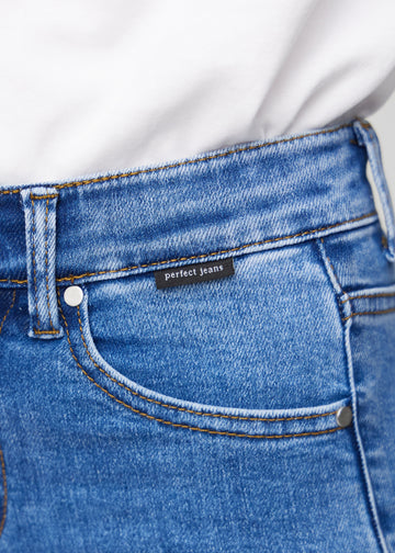Close-up of blue denim with the Perfect Jeans logo label at the edge of the front pocket.