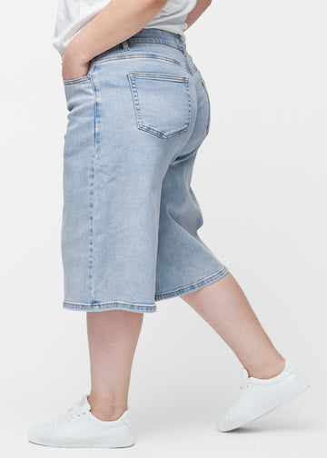 Loose, light blue denim capris in the colour Waves seen from the side on a plus-size model, where the wide fit and length to just below the knee are visible.