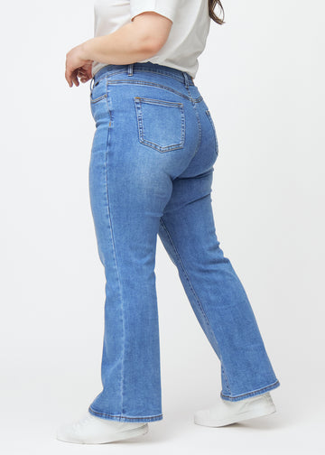Blå mid-rise bootcut jeans i denimfarven Rivers set fra siden på en plus-size model.