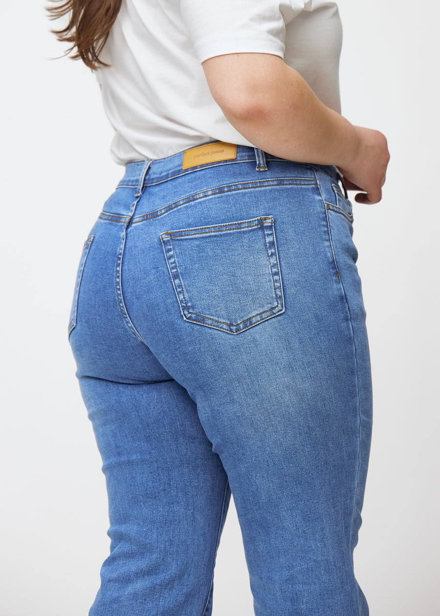 Blå mid-rise bootcut jeans i denimfarven Rivers set bagfra tæt på en plus-size model for at vise detaljer.