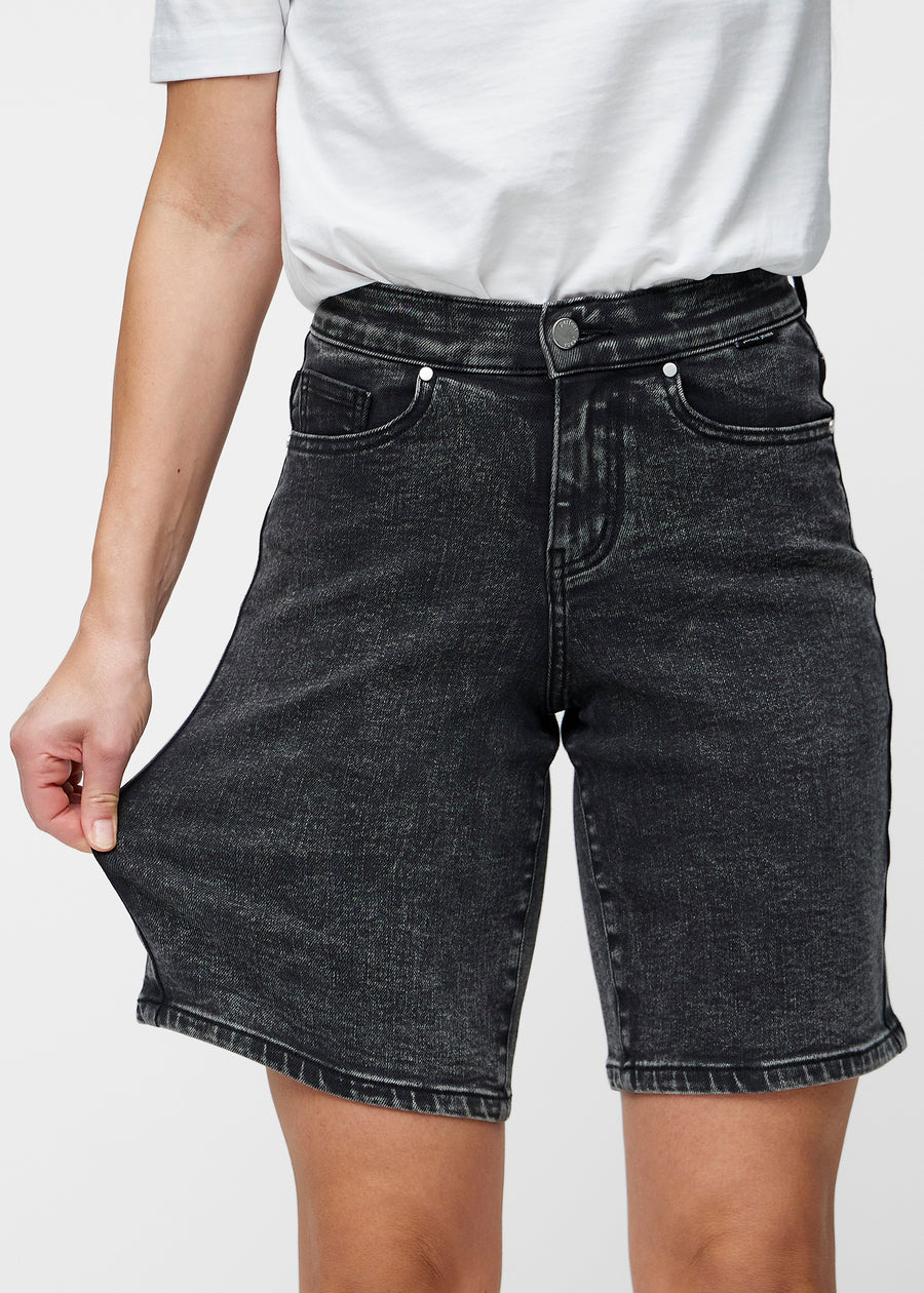 Model strækker de løse, mørkegrå denim shorts i farven Shadows ved hoften for at vise materialets stretch.