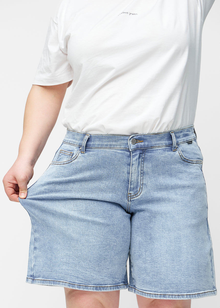 Plus-size model stretches the loose, light blue denim shorts in the colour Waves at the hips to show the material’s stretch.