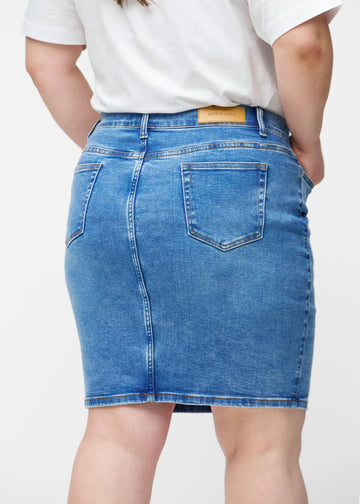 Klassisk blå, tætsiddende og knælang denimnederdel set bagfra tæt på på plus-size model for at vise detaljer.