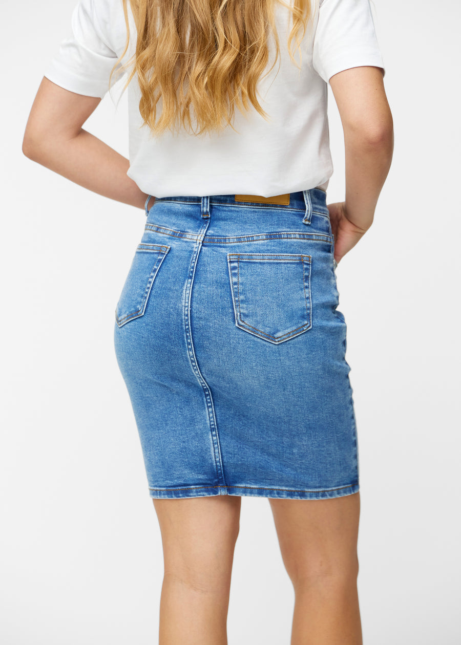 Klassisk blå, tætsiddende og knælang denimnederdel set bagfra tæt på for at vise detaljer.