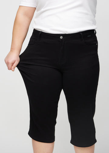 The plus-size model stretches the capris at the thigh to show the stretch.