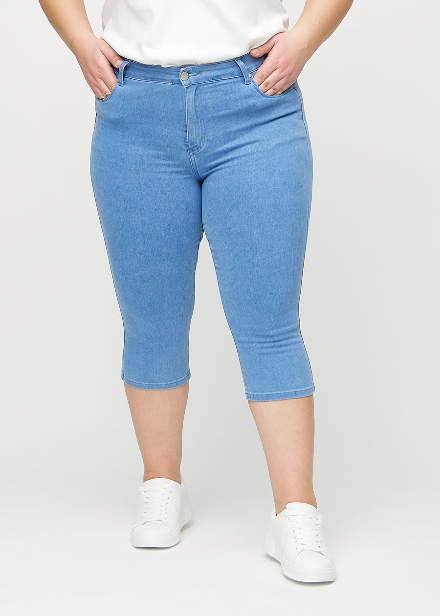 Blue skinny capris, model name Geraniums, which fit closely to the leg and end just below the knee on a plus-size model, seen from the front.