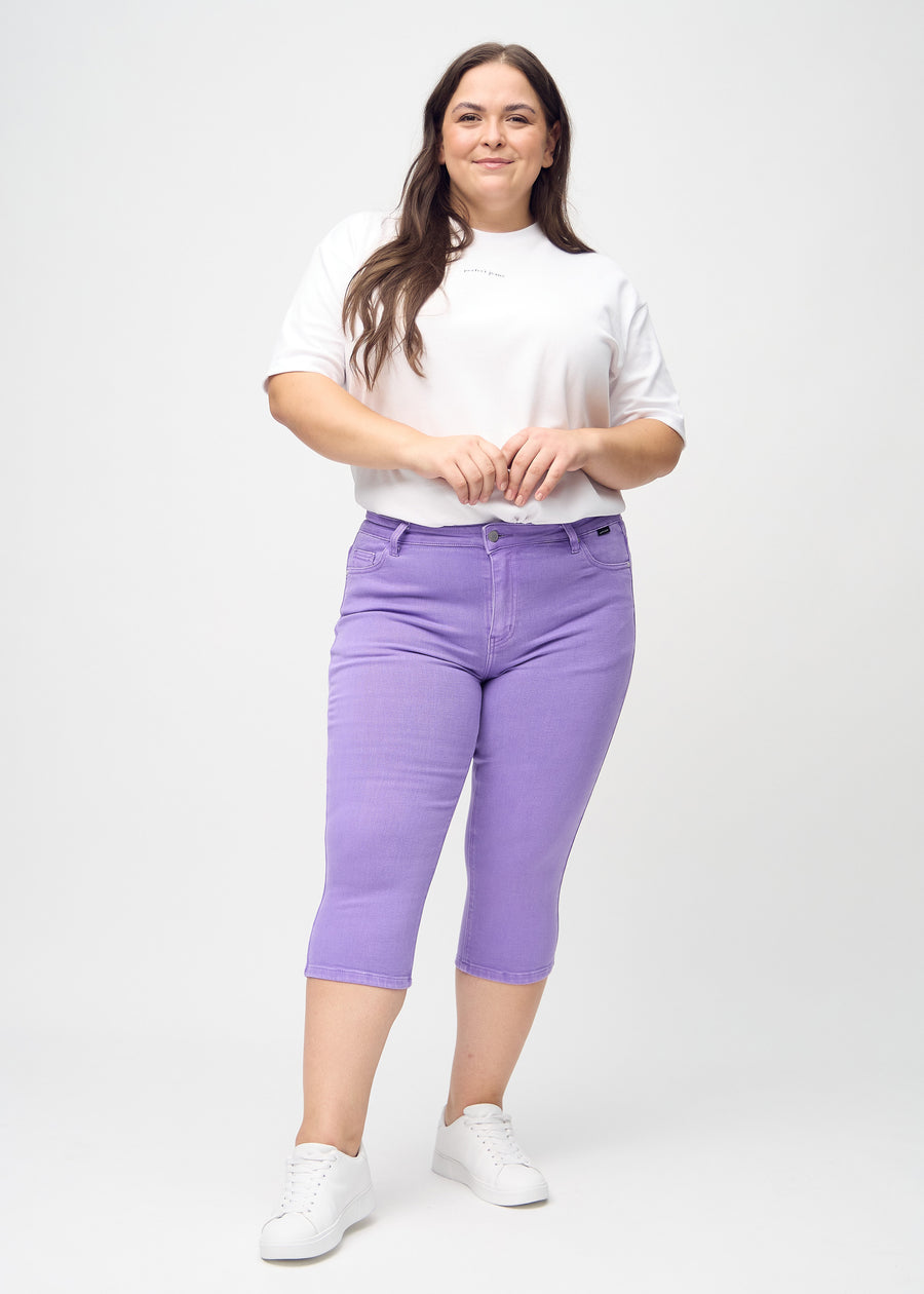 Skinny capris for women in pastel purple fabric, color Lavenders. Full-length view of a plus-size model wearing the capris.