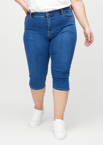 Dark denim skinny capris, model name Oceans, which fit close to the leg and end just below the knee on a plus-size model, seen from the front.