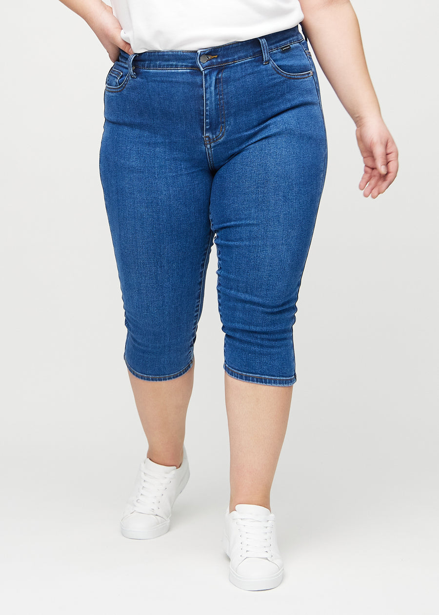Dark denim skinny capris, model name Oceans, which fit close to the leg and end just below the knee on a plus-size model, seen from the front.