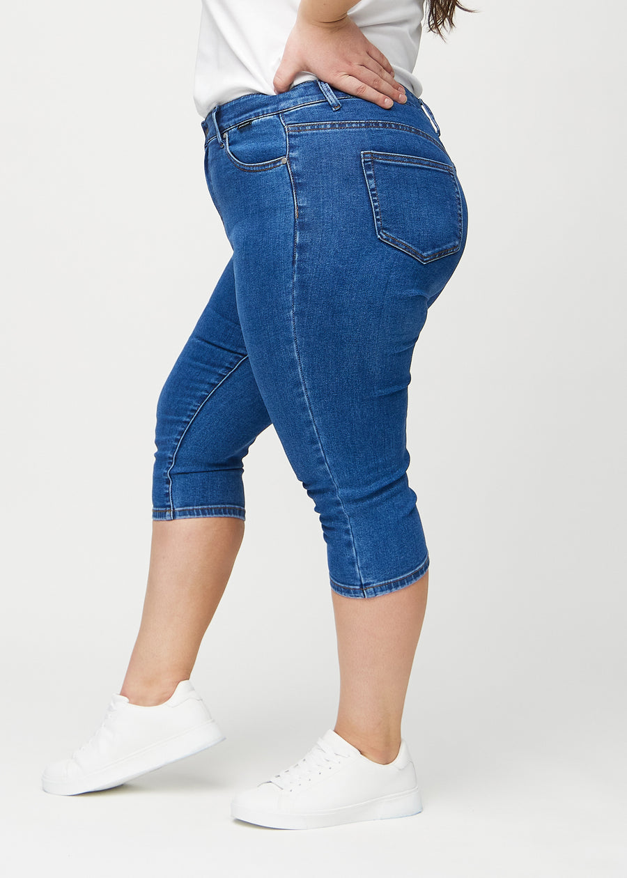 Dark denim skinny capris seen from the side on a plus-size model.