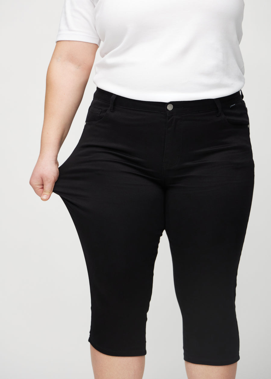 The plus-size model stretches the capris at the thigh to show the stretch.