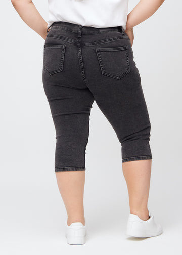 Dark grey denim skinny capris seen from the back on a plus-size model, so the entire product can be seen.
