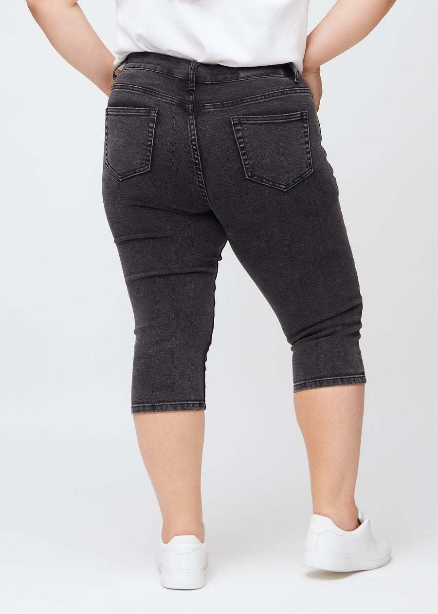 Dark grey denim skinny capris seen from the back on a plus-size model, so the entire product can be seen.