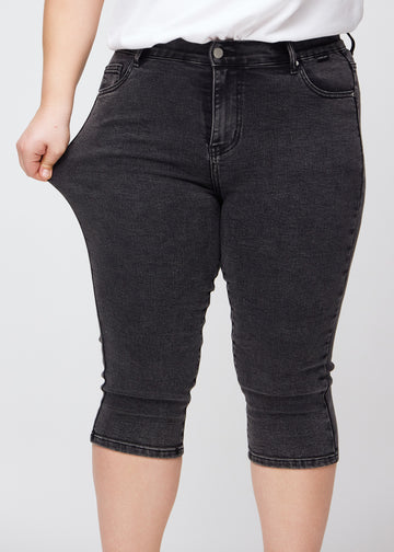 The plus-size model stretches the capris at the thigh to show the stretch.