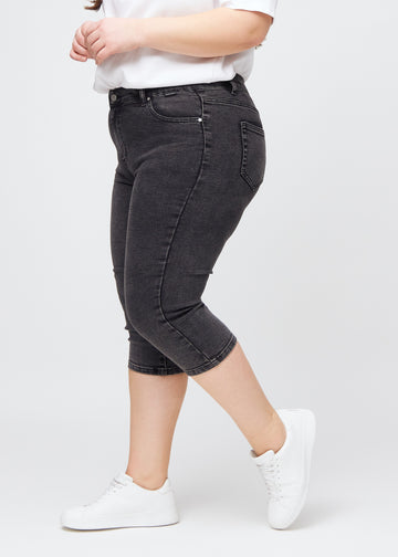 Dark grey denim skinny capris seen from the side on a plus-size model.