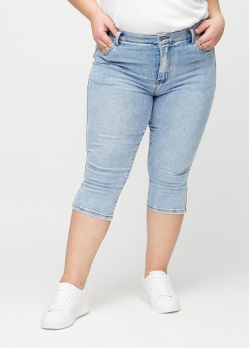 Light denim skinny capris, model name Waves, which fit closely to the leg and end just below the knee on a plus-size model, viewed from the front.