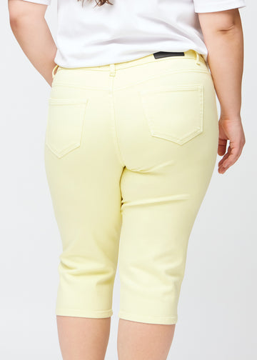 Close image of the back on a plus-size model in light yellow slim capris, detailed focus on pockets and stitching.