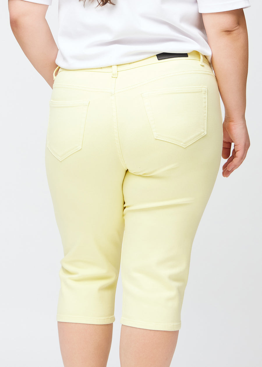 Close image of the back on a plus-size model in light yellow slim capris, detailed focus on pockets and stitching.