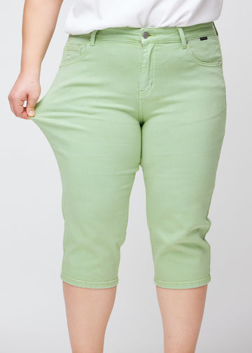 Slim capris for women in pastel light green jeans fabric, color Mints. A plus-size model pulls the fabric at the thigh to demonstrate stretch and flexibility.