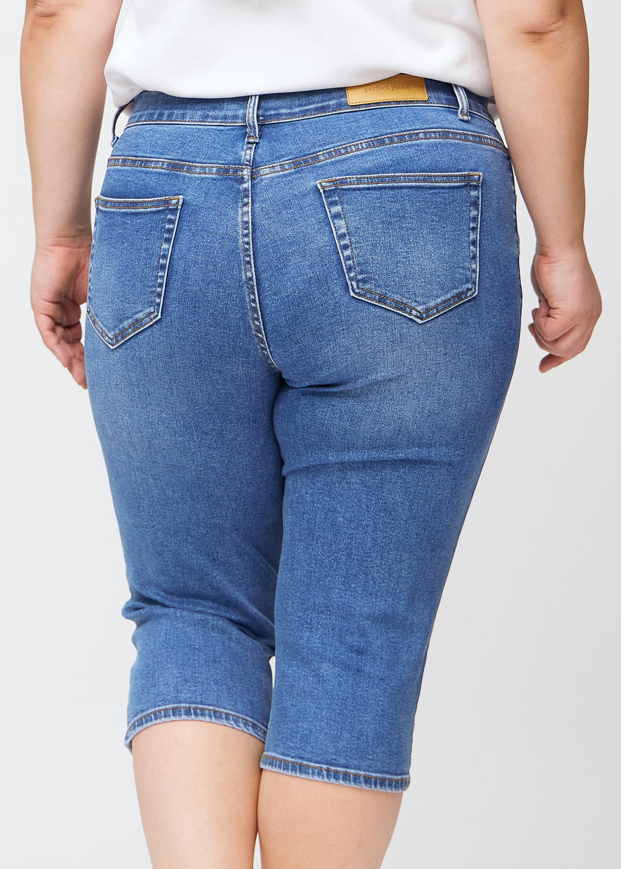 Slim capris for women in blue denim, color Rivers. Close-up from behind on a plus-size model, highlighting the back pockets and stitching.