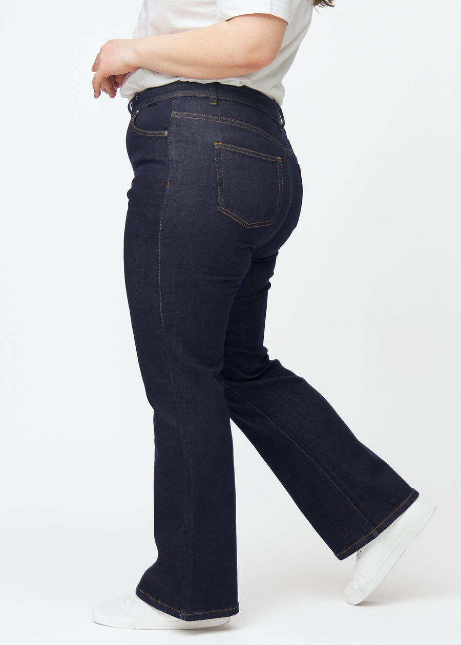 Deep dark blue denim jeans for women in the color Midnights with a bootcut fit seen from the side on a plus-size model.