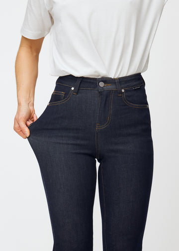The model stretches the deep dark blue denim jeans for women in the color Midnights at the thigh to show the material&