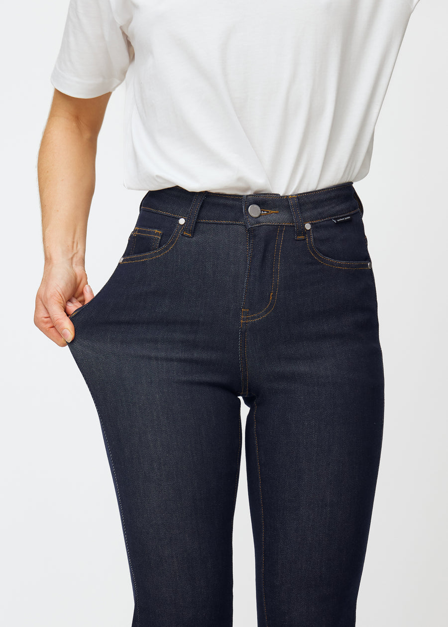 The model stretches the deep dark blue denim jeans for women in the color Midnights at the thigh to show the material&