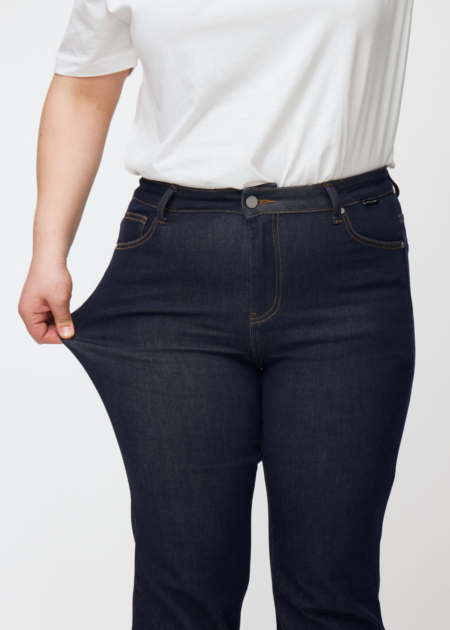 A plus-size model stretches the deep dark blue denim jeans for women in the color Midnights at the thigh to show the material&