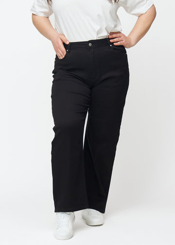Black high-waisted jeans in the Ravens model, which are fitted at the waist and have a loose fit with width down the leg, on a plus-size model shown from the front.