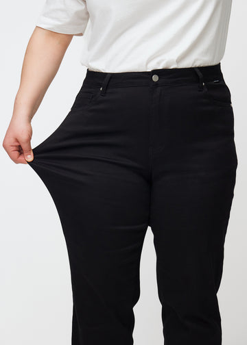 The plus-size model stretches the jeans at the thigh to show the stretch.