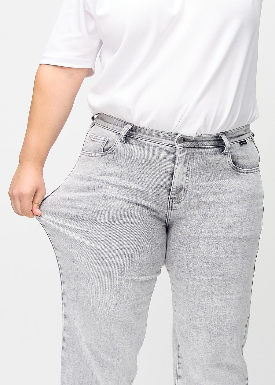 The plus-size model stretches the jeans at the thigh to show the stretch.