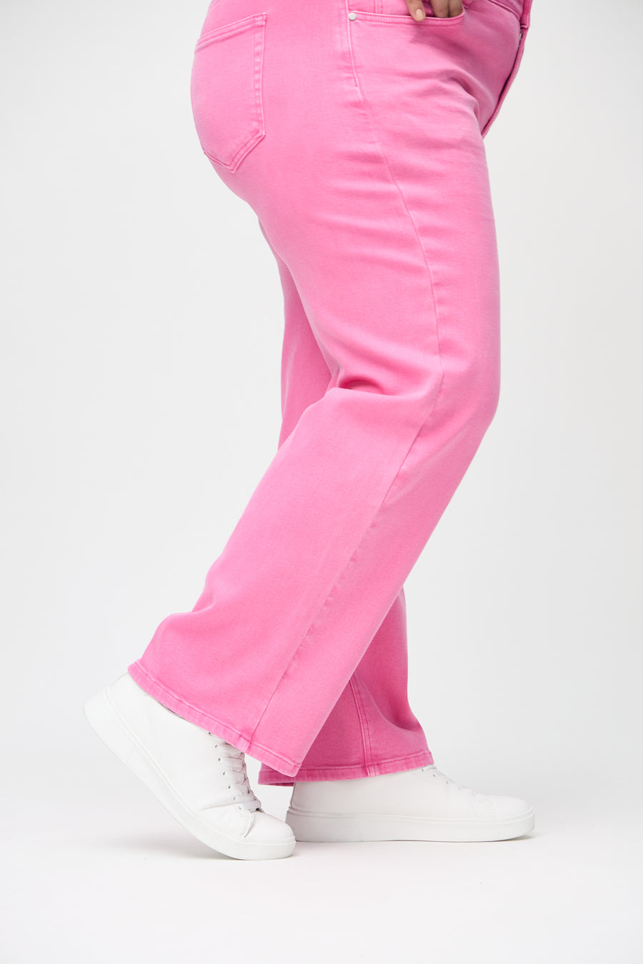 Loose jeans for women in light pink, color Flamingos. Close-up at the ankles on a plus-size model, showing the wide leg openings.