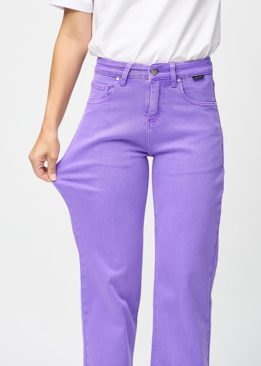 Loose jeans for women in purple, color Lavenders. A model stretches the denim at the thigh to show the fabric&