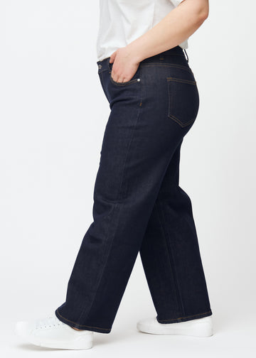 Deep dark blue denim jeans for women in the color Midnights with a loose fit, shown from the side on a plus-size model.
