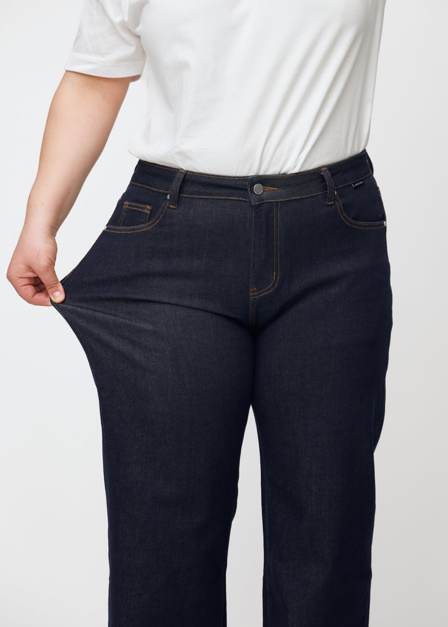 Plus-size model stretches the deep dark blue denim jeans for women in the color Midnights at the thigh to show the material&