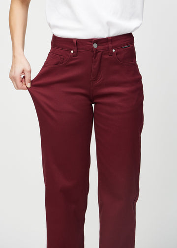 Loose jeans for women in dark red, color Santas. A model stretches the denim at the thigh to show the fabric&