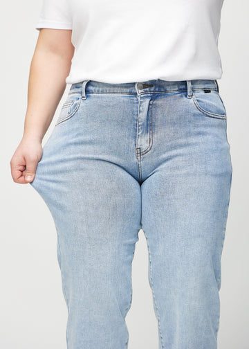 The plus-size model stretches the jeans at the thigh to show the stretch.