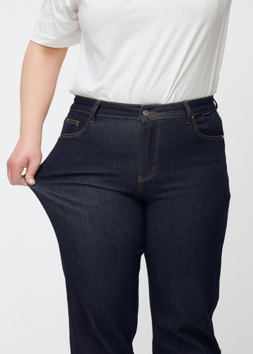 The plus-size model stretches the deep dark blue denim jeans for women in the color Midnights at the thigh to show the material&