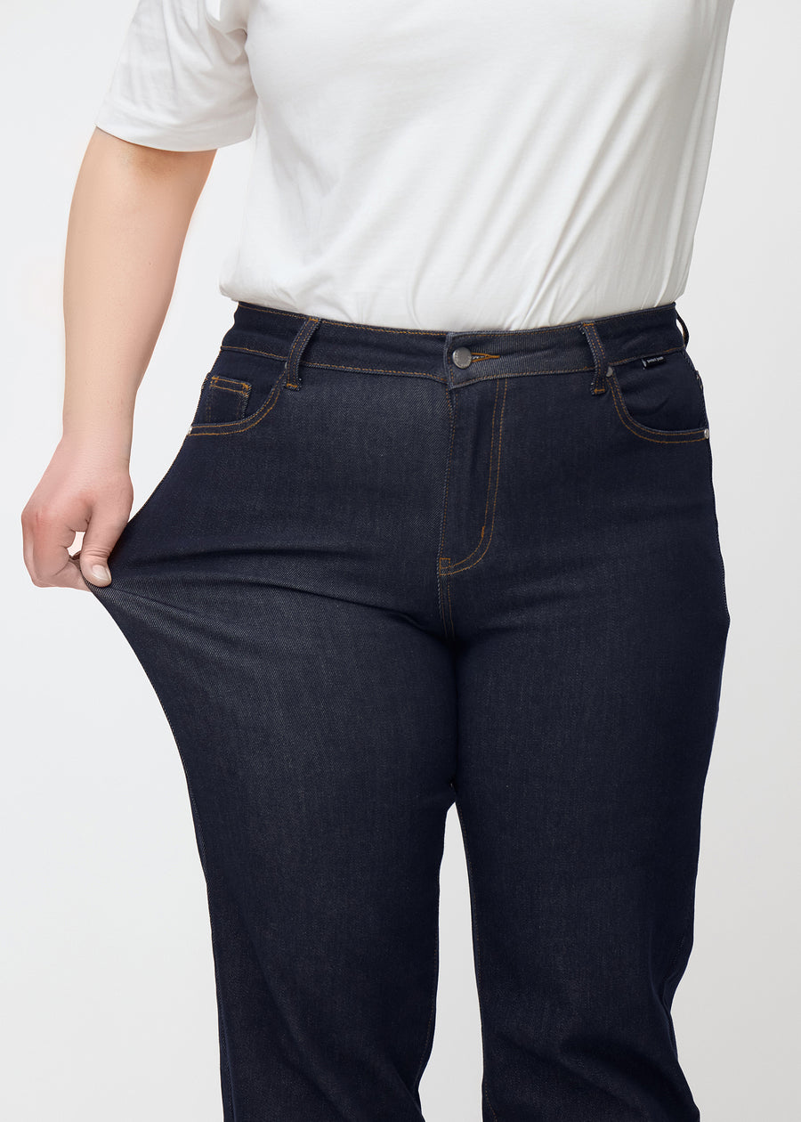 The plus-size model stretches the deep dark blue denim jeans for women in the color Midnights at the thigh to show the material&