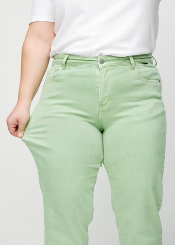 Regular jeans for women in light green, color Mints. A plus-size model stretches the fabric at the thigh to show its stretch.