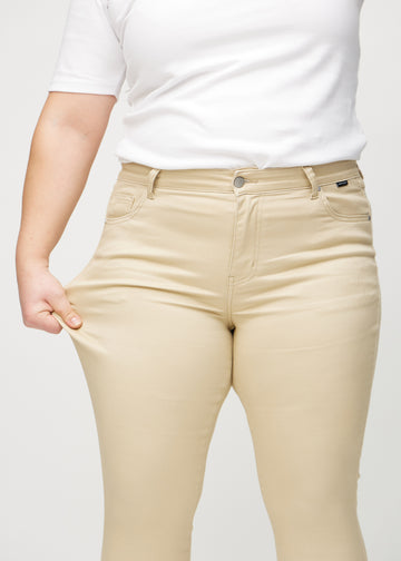Skinny jeans for women in beige, color Gazelles. A plus-size model stretches the jeans at the thigh to show the fabric&
