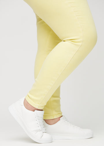 Skinny jeans for women in light yellow, color Lemonades. Close-up of the snug-fitting leg openings at the ankles on a plus-size model.