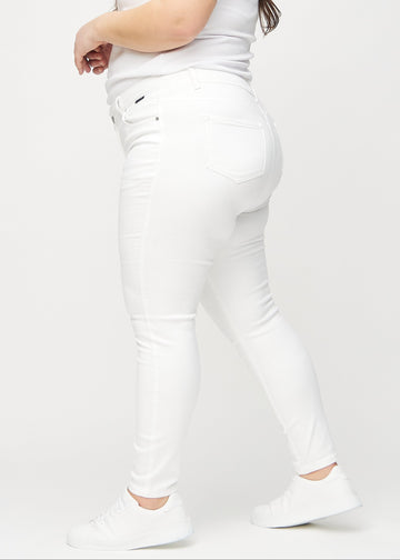 White skinny jeans seen from the side on a plus-size model.