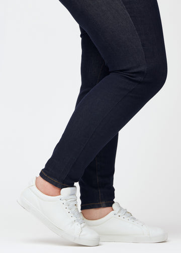 Deep dark blue denim jeans for women in the color Midnights with a skinny fit, shown close up at the ankles on a plus-size model to display the close-fitting finish.