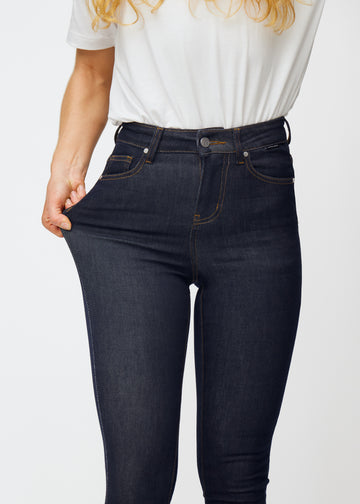The model stretches the deep dark blue denim jeans for women in the color Midnights at the thigh to show the material&