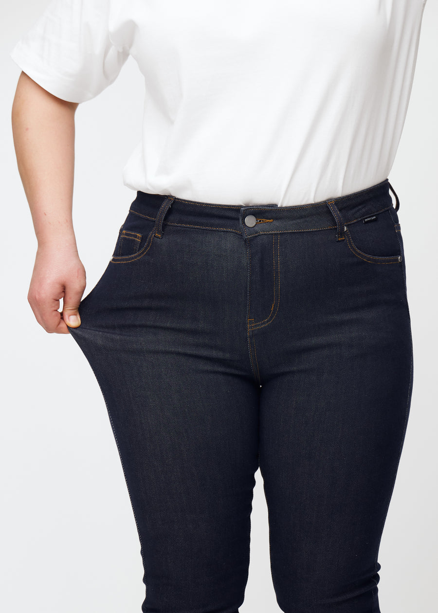 A plus-size model stretches the deep dark blue denim jeans for women in the color Midnights at the thigh to show the material&