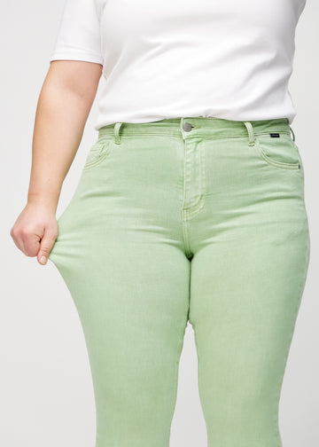 Skinny jeans for women in light green, color Mints. A plus-size model stretches the jeans at the thigh to show the fabric&